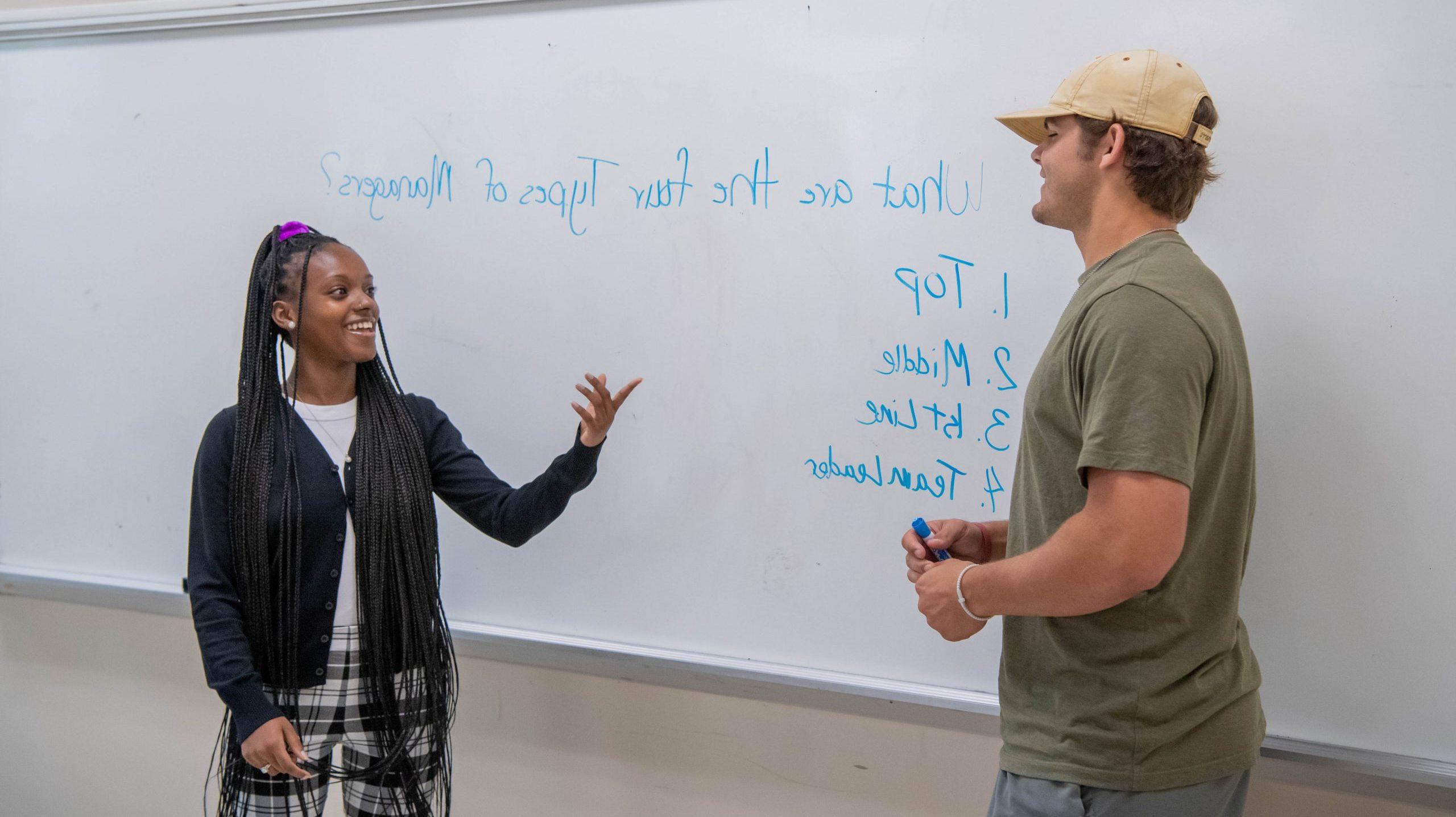 A male and female student listing the four types of managers on a whiteboard.