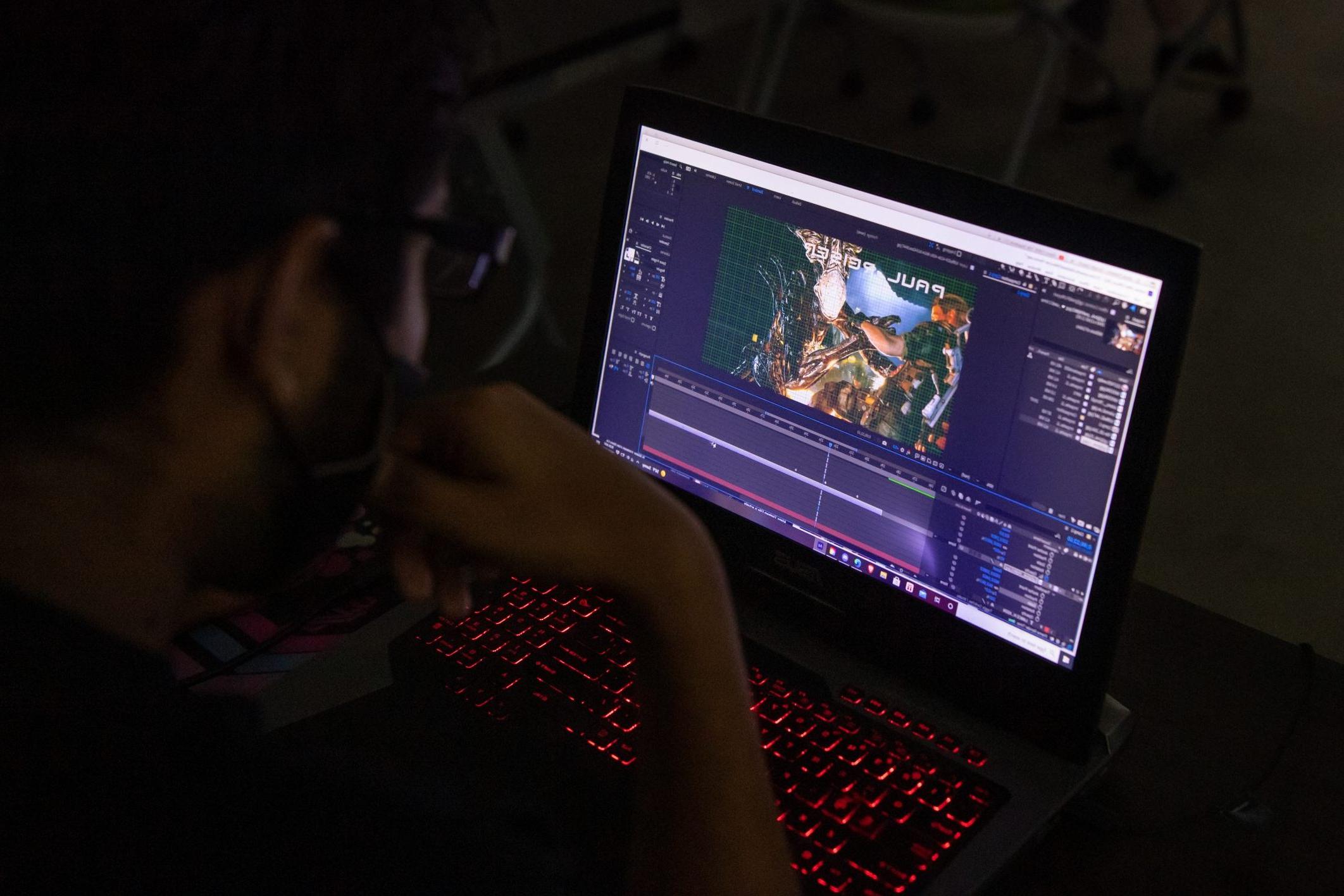 Student sitting in the dark on a laptop working on Animation assignment